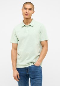 Jasnozielona koszulka polo z krótkim rękawem, trzema guzikami i subtelną teksturą w paski. W połączeniu z niebieskimi dżinsami.