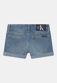 Vaaleansiniset farkkushortsit, joissa on käännetty helma ja kaksi takataskua, joissa on erottuvat ompelukuvioinnit. Calvin Klein Jeans -merkki vyötärönauhassa.