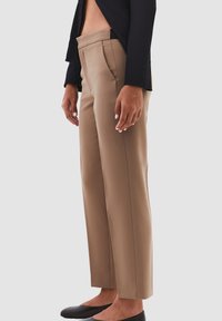 Beige op maat gemaakte broek met een rechte pijp, zijzakken en een gladde, lichte stof. Gecombineerd met zwarte flats en een donkere top.