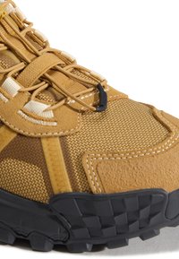 Gros plan d'une chaussure de randonnée marron et beige avec tissu en maille, panneaux en suède, lacets élastiques et semelle en caoutchouc noir à crampons.