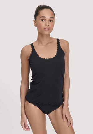 Vrouw in een zwarte cami met kant en bijpassend ondergoed tegen een eenvoudige lichte achtergrond.