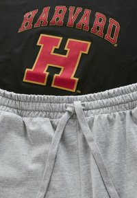 Čierne tričko s odvážnym nápisom "HARVARD" v červenej a zlatej farbe, doplnené sivými teplákmi s elastickým pásom a šnúrkou.