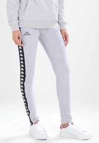 Grå sweatpants med en åtsittande design, prydda med svarta sidosträck och en logotypmönster. Tillverkade av mjukt material, ihop med vita sneakers.