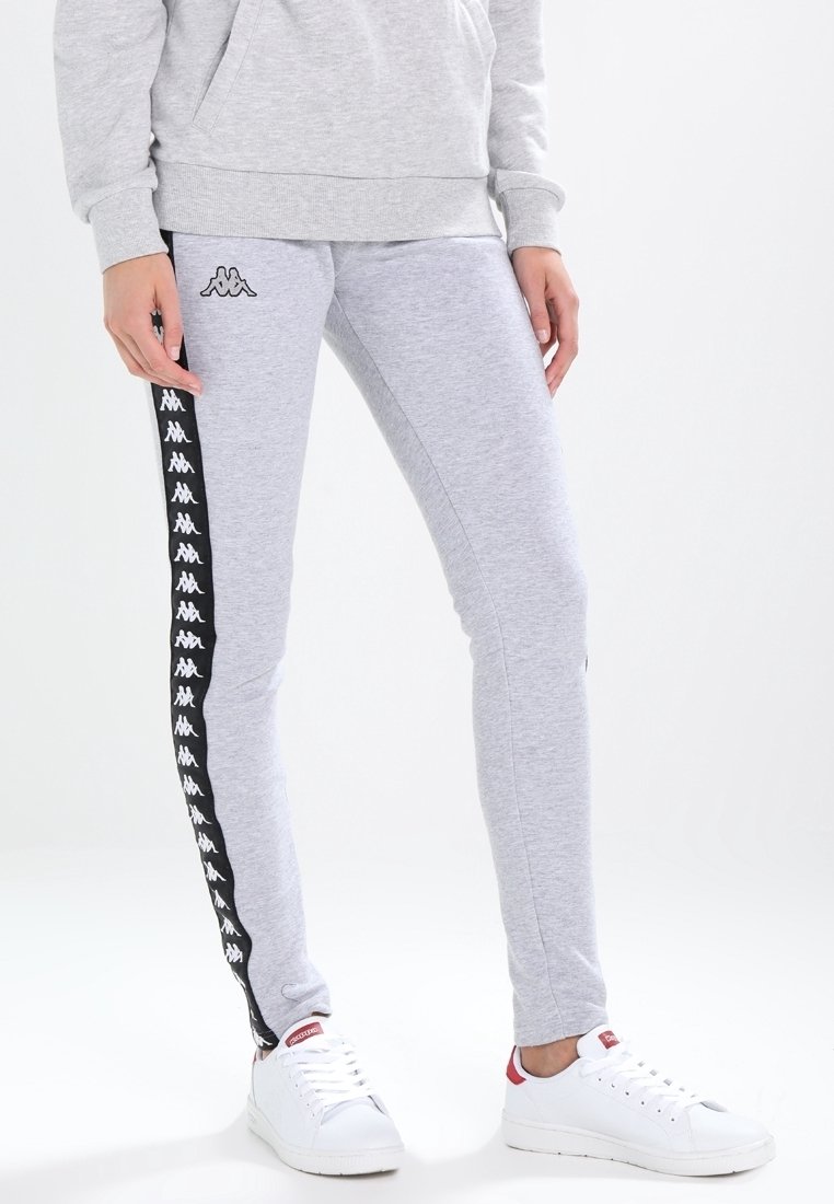 Grå sweatpants med en åtsittande design, prydda med svarta sidosträck och en logotypmönster. Tillverkade av mjukt material, ihop med vita sneakers.