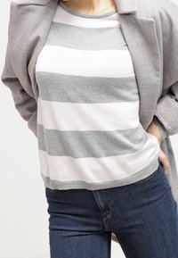 Un haut à manches courtes rayé gris clair et blanc, avec un col rond, associé à un jean bleu foncé. Un tissu doux avec une coupe décontractée.