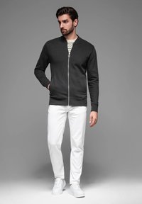Sudadera negra con cremallera y cuello redondo, combinada con pantalones blancos y zapatillas blancas. Textura suave, diseño minimalista, ajuste casual.