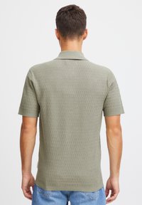 Strukturert grønn kortermet polo skjorte med strikket mønster og ribbestrikket krage. Båret over blå jeans, som viser et avslappet snitt.