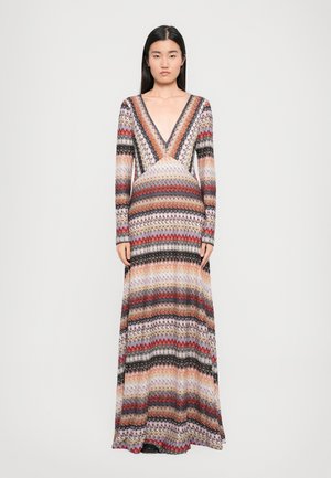 Maxime dress with long sleeves, deep V-neck, and multicolored zigzag pattern in shades of red, black, and cream. Crafted from lightweight knitted fabric.