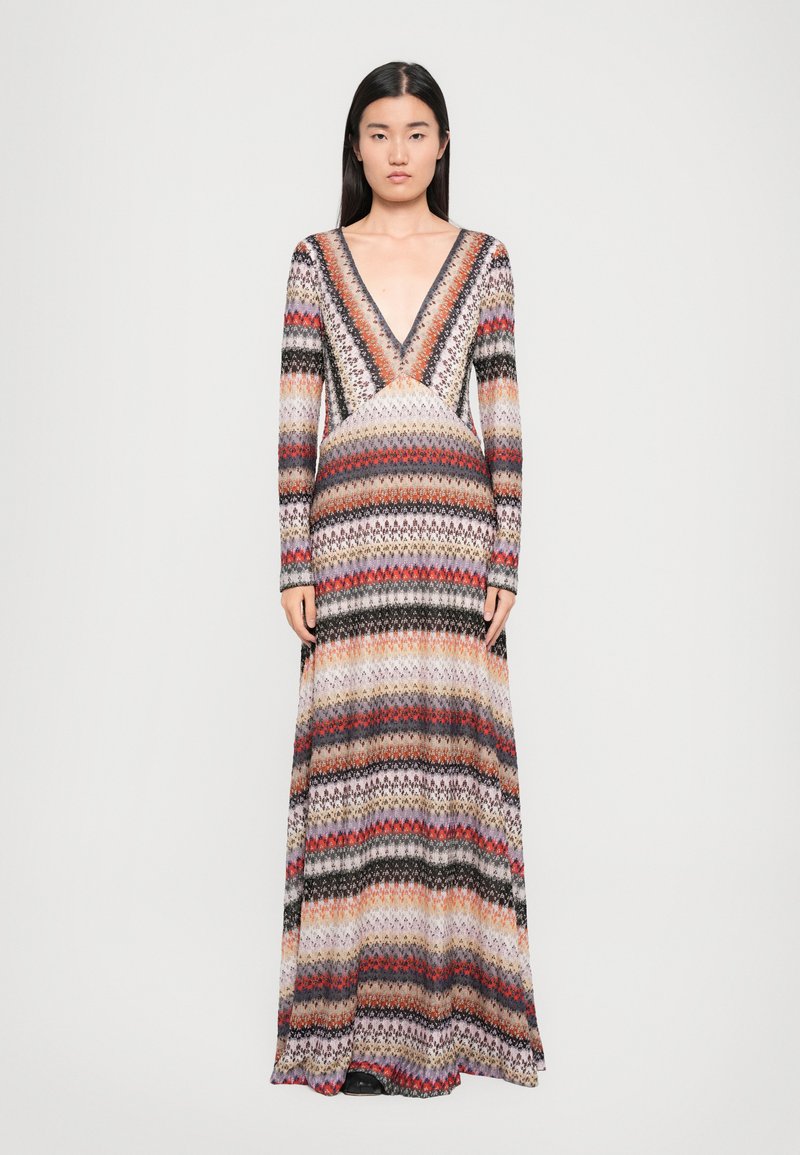 Maxi suknelė su ilgomis rankovėmis, giliu V formos iškirpimu ir daugiaspalviu zigzago raštu raudonos, juodos ir kreminės spalvų atspalviais. Pagaminta iš lengvos mezginio medžiagos.