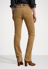 Pantaloni di velluto a coste color sabbia con una vestibilità slim, dotati di tasche posteriori e una finitura testurizzata. Abbinati a stivali con tacco marroni.