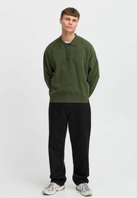 Grønn strikket genser med krage, med tre knapper, kombinert med løse sorte bukser og lyse sneakers. Glatt tekstur.
