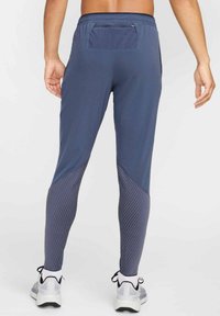 Granatowe spodnie sportowe z gładką górną częścią i pasującą dolną częścią w paski. Zawierają kieszeń z tyłu oraz dopasowany krój. Akcenty z teksturowanej tkaniny.