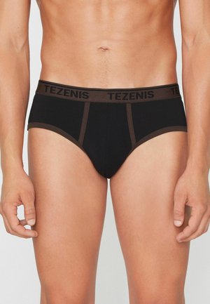Torso masculino que lleva calzoncillos negros con una cintura y ribete marrones, con la marca "TEZENIS" en la cintura.