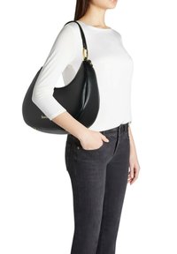 Borsa hobo in pelle nera con silhouette curva, caratterizzata da un dettaglio dorato e una tracolla, tenuta da una persona con una maglietta bianca e jeans scuri.