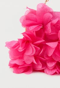 Fleurs en tissu rose vif densément regroupées sur un accessoire chaîne dorée sur fond blanc uni.