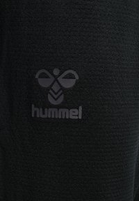 Nahaufnahme von schwarzem Stoff, der eine glatte Textur aufweist und ein prominentes Hummel-Bienenlogo in einem dunkleren Schwarz zeigt.