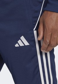 Navy träningsbyxor med vita sidostråk och en broderad vit logotyp. Slät textur, taperad design och åtsittande vid midjan.