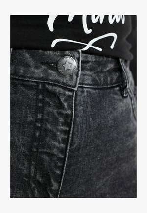 Jeans in denim nero con una leggera brillantezza, caratterizzati da un bottone metallico con design a stella e un tessuto testurizzato. Vista ravvicinata dell'area della cintura.