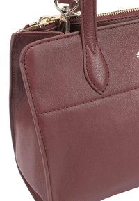 Bordeaux leren handtas met een gestructureerde vorm, voorzien van gouden hardware, een ritssluiting en dubbele handvatten bovenaan. Textuur oppervlak met stiksels.