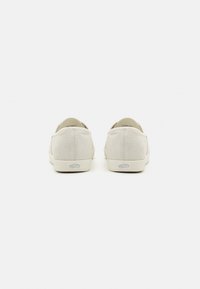 White suede slip-on shoes with a textured finish, rounded toe, and cream sole, featuring a small logo on the back.