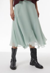 Muntgroene, vloeiende chiffon rok met een golvende zoom, gecombineerd met zwarte leren enkelboots met zilverkleurige hardware en een chunky hak.