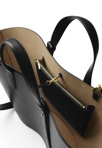 Sort læder tote bag med en glat overflade, åben top, lys brun ruskindsforing og en lynlåslomme indeni med guldfarvede hardware detaljer.