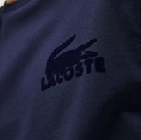 Póler de marina con tejido de algodón texturizado que presenta un logotipo de cocodrilo en azul oscuro bordado y el texto "LACOSTE" en el frente.