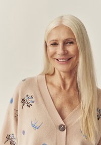 Heleroosa kardigan lille- ja linnu tikandiga, sügava V-kaelusega ja esiküljel dekoratiivse nööbiga. Pehme tekstuur.