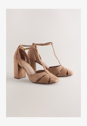 Semiš čevlji z visokimi petami v barvi opečnato rjave, s T-trakom, odprtimi prsti in geometrijskimi izrezi. Imajo robustno blok peto za podporo.