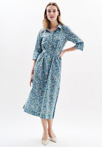 Robe à boutons florale bleu avec des accents verts et jaunes, dotée de manches trois-quarts, d'une taille ceinturée et d'une coupe mi-longue.