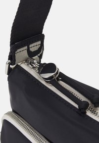 Borsa in tessuto nero con due cerniere argento, dotata di una tracolla texturizzata e dettagli delle cerniere di colore chiaro in contrasto. Materiali lisci e resistenti.