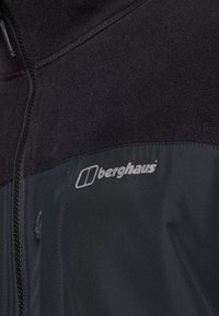 Giacca nera con chiusura a zip, caratterizzata da una parte superiore texturizzata e una sezione inferiore liscia. Presenta un logo "Berghaus" argento sul petto.