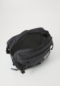 Zaino nero con scomparto principale con zip, realizzato in tessuto resistente. Dotato di spallacci regolabili e una piccola tasca frontale.