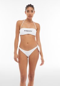 Valkoinen bikinit-setti, jossa on bandeau-toppi etuosan logolla ja sivusolmittavat alaosat, virtaviivainen muotoilu, sileä pinta ja minimalistinen tyyli.