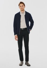 Granatowy sweter kardigan na górę jasnoszarej koszuli z guzikami, czarne spodnie i szare botki za kostkę. Gładka faktura bez widocznych wzorów czy ozdób.