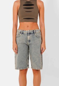 Pantalones cortos de vaquero tipo bermuda, de lavado claro, con un corte relajado y dobladillo deshilachado. Combinados con una parte superior marrón corta con diseño de cortes.