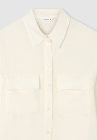 Blusa bianca realizzata in tessuto liscio, con colletto, chiusura anteriore a bottoni e due tasche sul petto. Texture morbida, design minimalista.