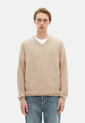 Beige v-hals sweater lavet af blødt stof, med lange ærmer og ribbet halsudskæring, parret med lyseblå jeans. Delikat logo detalje.