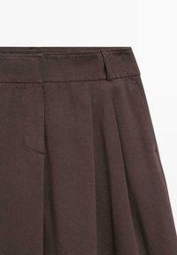 Brązowa plisowana spódnica o gładkiej fakturze, z paskiem w talii i bocznymi kieszeniami, wykonana z lekkiego materiału.