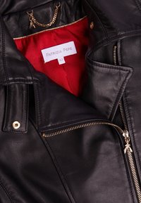 Mustan nahkatakin kultaisilla yksityiskohdilla, punaisella satiinivuorella ja etiketillä, jossa lukee "PATRIZIA PEPE, 42." Takissa on edessä täyspitkä vetoketju ja kaulustyyli.