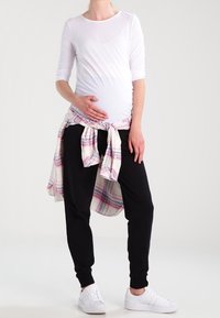 White long-sleeve top, black jogger pants, and a tied plaid shirt around the waist. White sneakers complete the outfit.