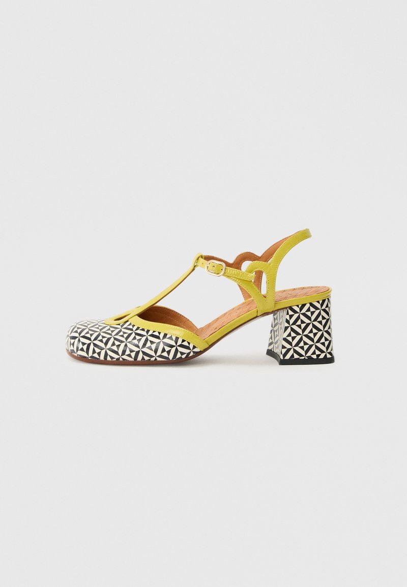 Gule slingback-sko med T-rem design, der har en geometrisk sort-hvid mønstret tå og en chunky hæl med et matchende mønster.