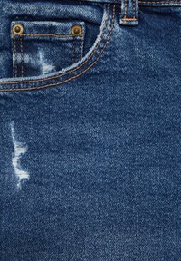 Blå denimtyg med en sliten mönster, synlig sömnad, en liten frampocket med mässingsdetaljer och en texturerad yta.