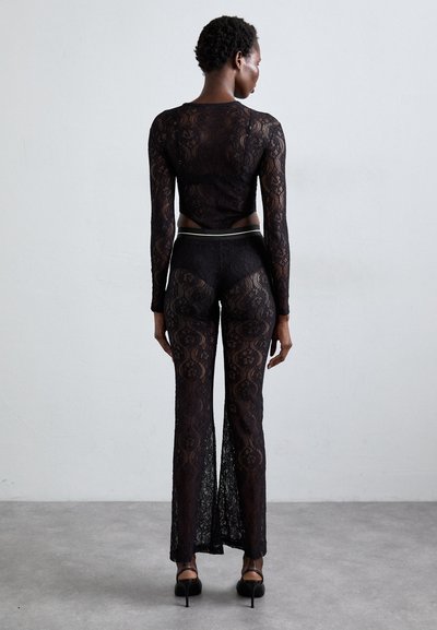 Black lace outfit featuring a long-sleeve top and high-waisted pants with a sheer design, textured floral pattern, and side slits.