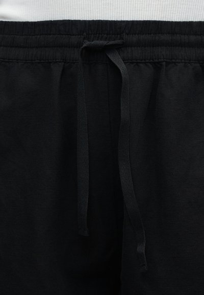 Μαύρη ελαστική μέση με δεμένο κορδόνι σε μαύρο παντελόνι, το πάνω άκρο δείχνει μέρος ενός λευκού πουκάμισου πάνω από τη μέση.