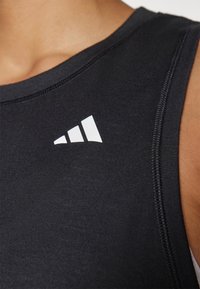 Czarny sportowy top na ramiączkach z okrągłym dekoltem, z białym logo po lewej stronie oraz gładką, elastyczną teksturą materiału.