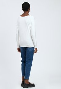 Maglietta bianca a maniche lunghe con scollatura rotonda, abbinata a jeans di denim blu con leggere abrasioni sul tessuto. Scarpe nere completano il look.