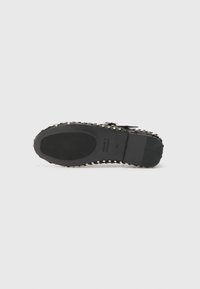 Semelle de chaussure noire avec grip en caoutchouc, ornée de clous métalliques tout autour du bord, présentant une finition lisse et une légère courbure à l'avant.
