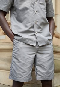 Grå kortärmad skjorta och matchande shorts gjorda av ett mjukt material. Skjortan har en framficka och knappar, medan shortsen har rak skärning.