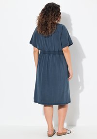 Polvisyvän, tummansinisestä puuvillasta valmistettu mekko, jossa on leveät hihat, joustava vyötärö ja rento leikkaus. Mekon pinta on sileä ja yksityiskohtia on vain minimaalisti.